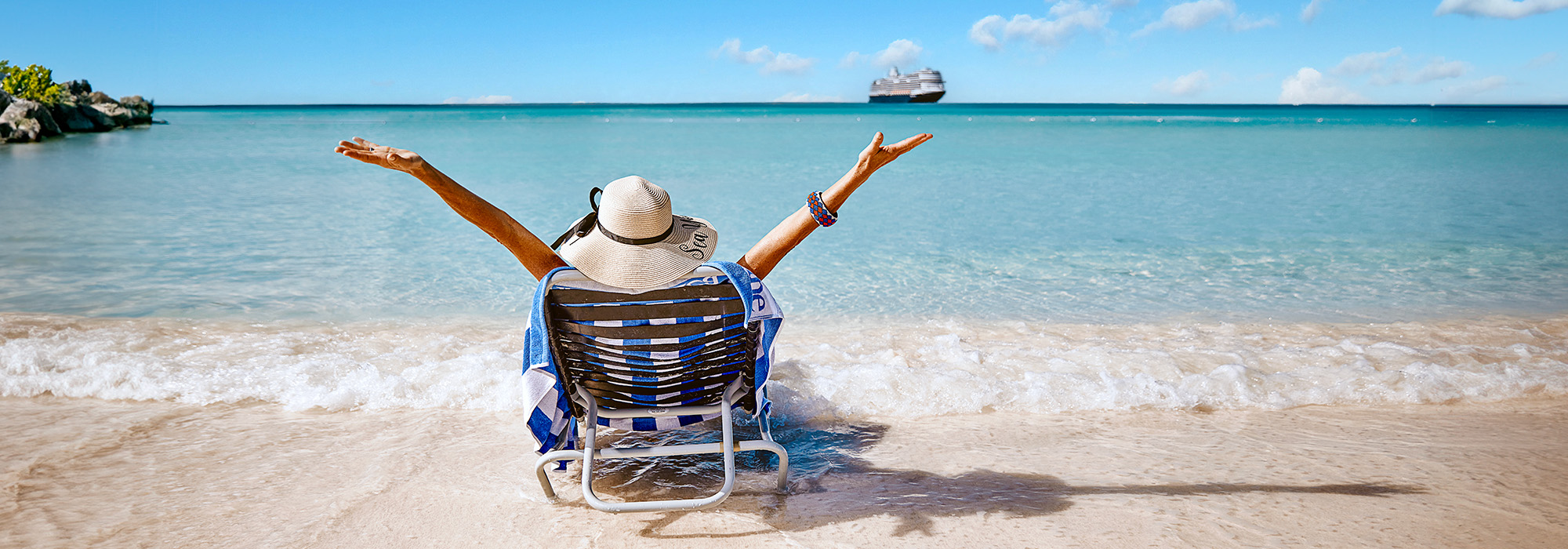 Lady sunbathing on beach at Half Moon Cay, with Holland America ship anchored
