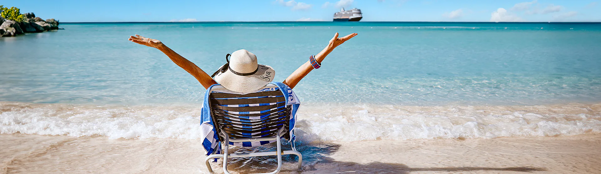Lady sunbathing on beach at Half Moon Cay, with Holland America ship anchored