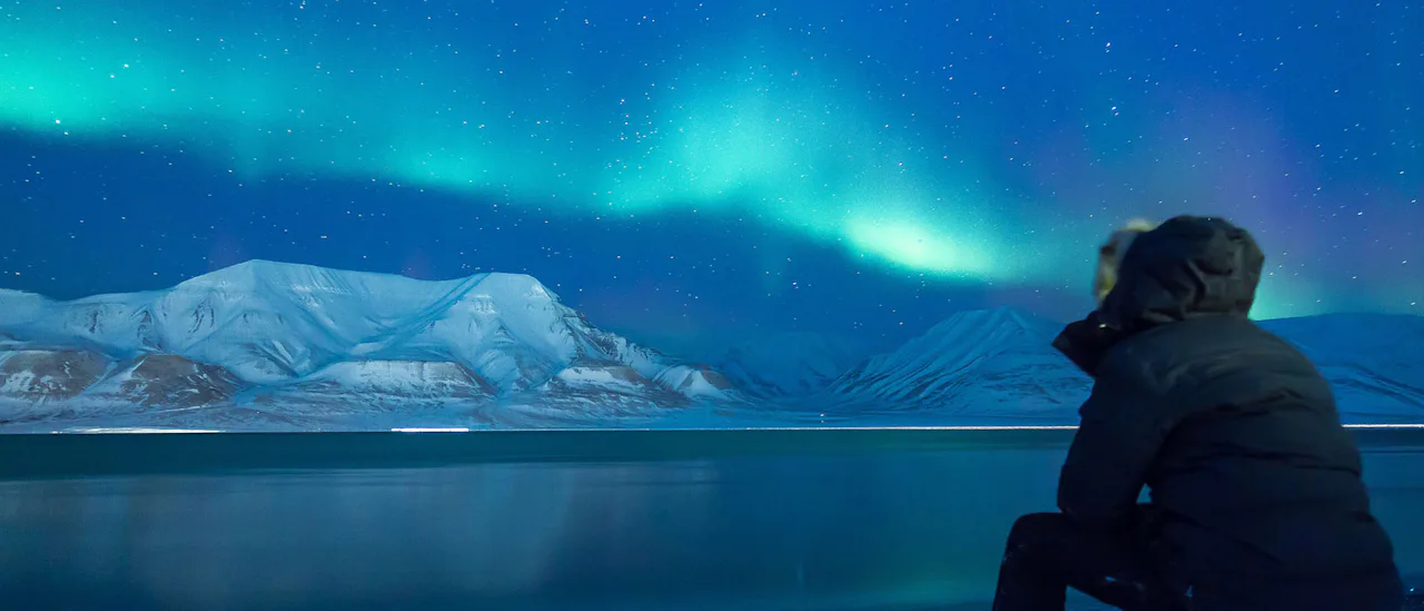 Person watching the Aurora Borealis dancing above the mountains