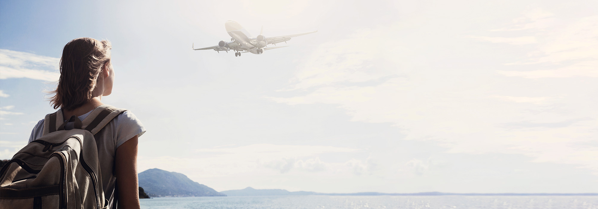 Woman near sea watching a plane
